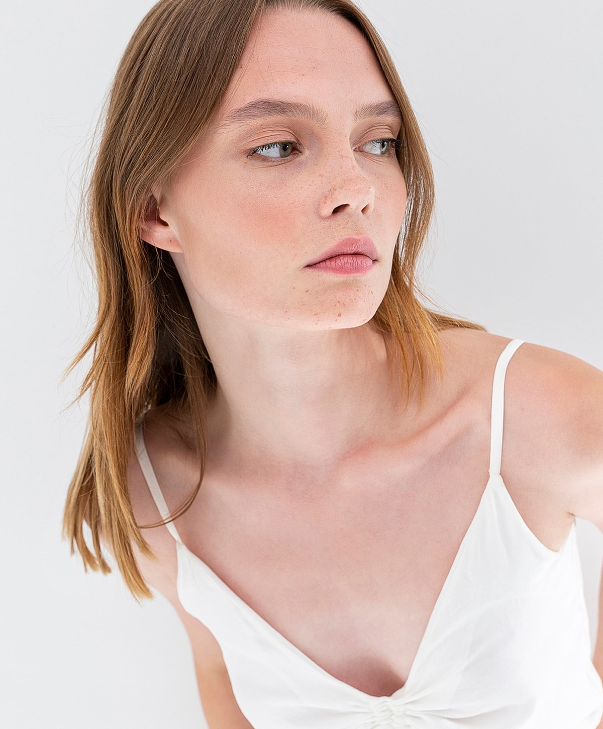Model in white top, looking thoughtfully to side.